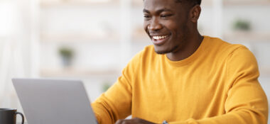 Boy in yellow t-shirt working on a laptop and smiling